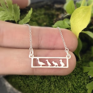 Może przedstawiać: Srebrny naszyjnik z prostokątnym wisiorkiem przedstawiającym wycięty wzór czterech gęsi w rzędzie.