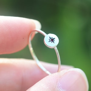 May include: A silver ring featuring a small, round, red gemstone set in a star-shaped design.