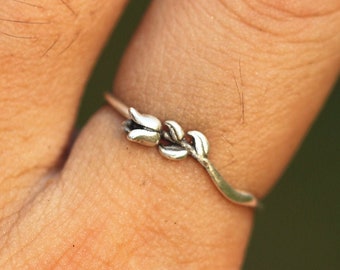 May include: A silver ring featuring a delicate floral design. The ring is worn on the middle finger of a hand.