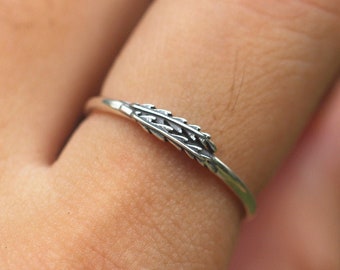May include: A silver ring with a delicate wheat design. The ring is worn on a finger.