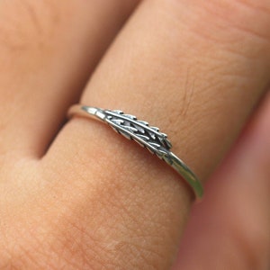 Puede incluir: Un anillo de plata con un delicado diseño de trigo. El anillo se lleva en un dedo.