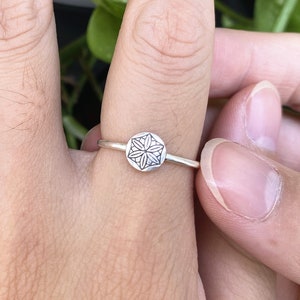 Op de afbeelding: Een zilveren ring met een geometrisch ontwerp op de band. Het ontwerp is een cirkelvormige mandala met een bloemvormig patroon.