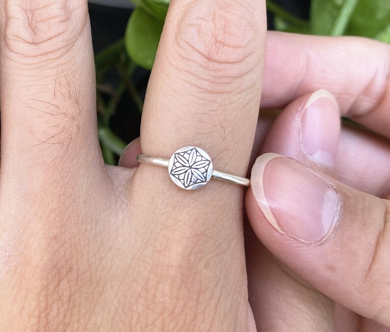 Op de afbeelding: Een zilveren ring met een geometrisch ontwerp op de band. Het ontwerp is een cirkelvormige mandala met een bloemvormig patroon.