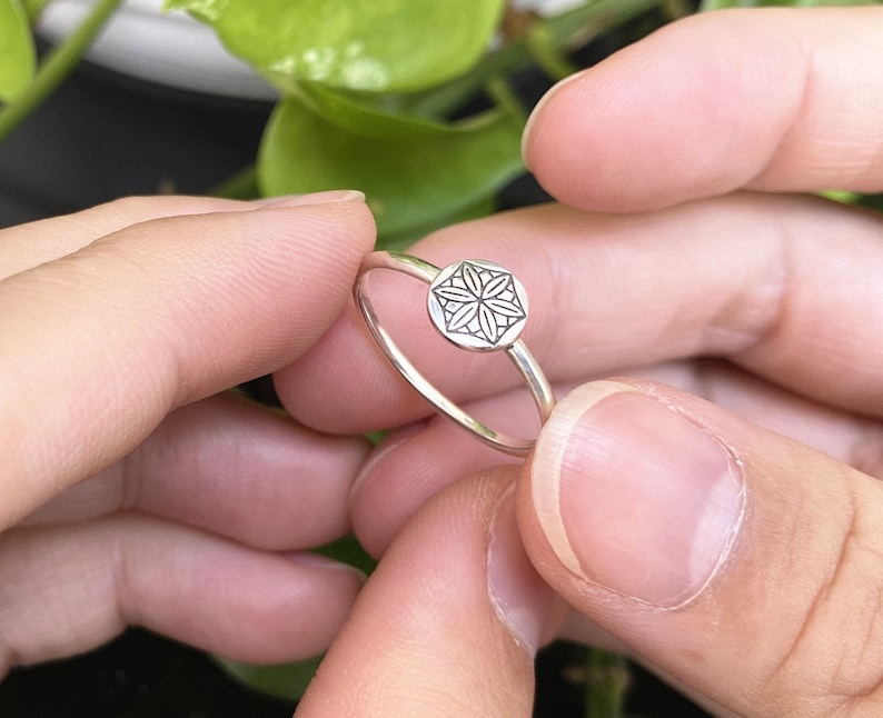 Op de afbeelding: Een zilveren ring met een geometrisch ontwerp aan de bovenkant. De ring zit aan een vinger.