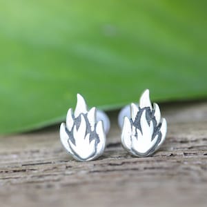 Puede incluir: Un par de pendientes de plata con un diseño de llama. Los pendientes son pequeños y delicados, y serían un gran regalo para alguien que ama el fuego.