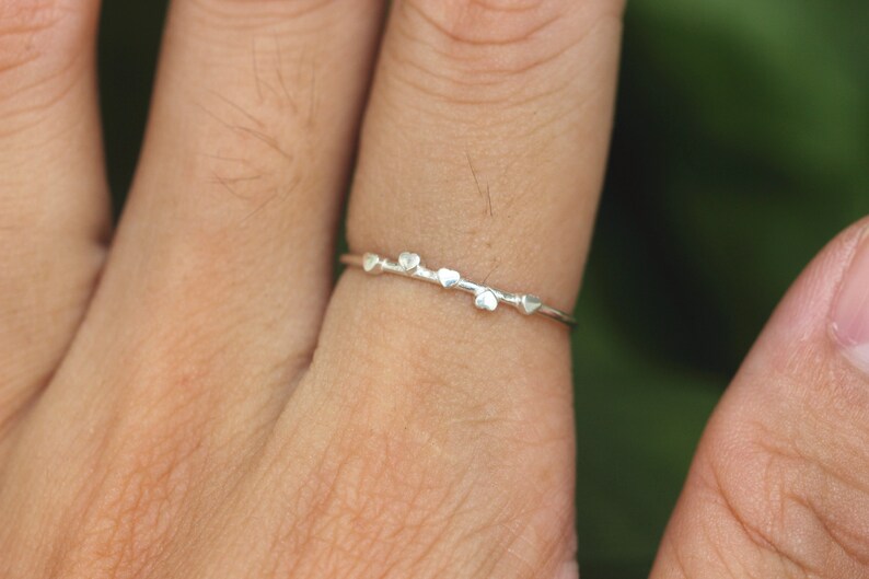 K&ouml;nnte beinhalten: Ein silberner Ring mit einem zarten Design aus f&uuml;nf kleinen Herzen.
