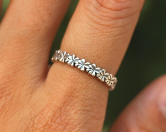 Op de afbeelding: Een zilveren ring met een delicaat ontwerp van kleine bloemetjes rond de band.