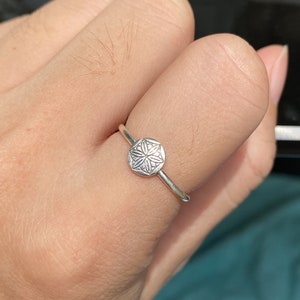 May include: A silver ring with a circular design featuring a detailed floral pattern.