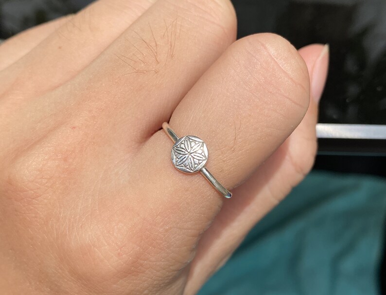 May include: A silver ring with a circular design featuring a detailed floral pattern.