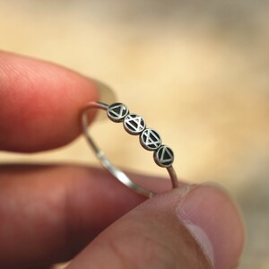 May include: A silver ring with five small circles, each with a black triangle design.