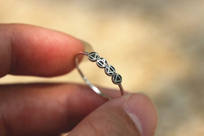 May include: A silver ring with five small circles, each with a black triangle design.