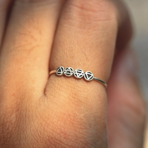 May include: A silver ring featuring five small circles, each with a distinct geometric symbol. The symbols are arranged in a line.
