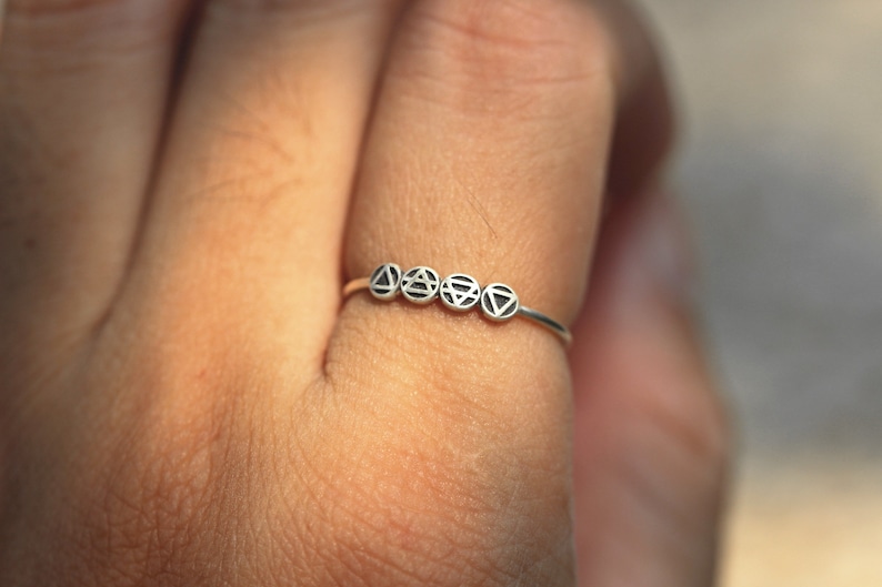 May include: A silver ring featuring five small circles, each with a distinct geometric symbol. The symbols are arranged in a line.
