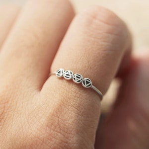 May include: A silver ring featuring five small circles, each with a distinct geometric design. The ring is worn on a finger.