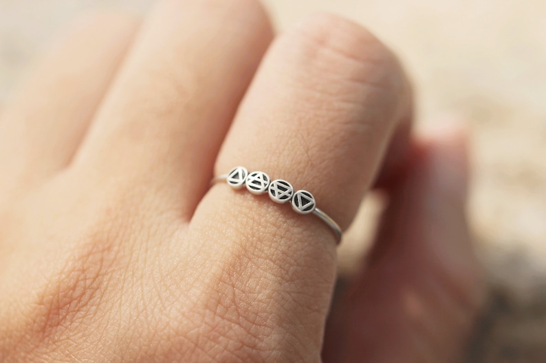 May include: A silver ring featuring five small circles, each with a distinct geometric design. The ring is worn on a finger.