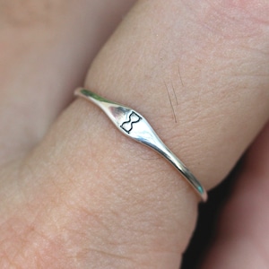 May include: A silver ring with a bow tie design. The ring is worn on a finger.