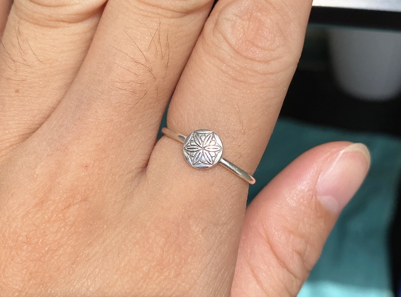 May include: A silver ring with a delicate, circular design featuring a stylized flower motif.