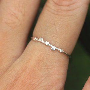K&ouml;nnte beinhalten: Ein silberner Ring mit einem zarten Band und f&uuml;nf kleinen herzf&ouml;rmigen Anh&auml;ngern.