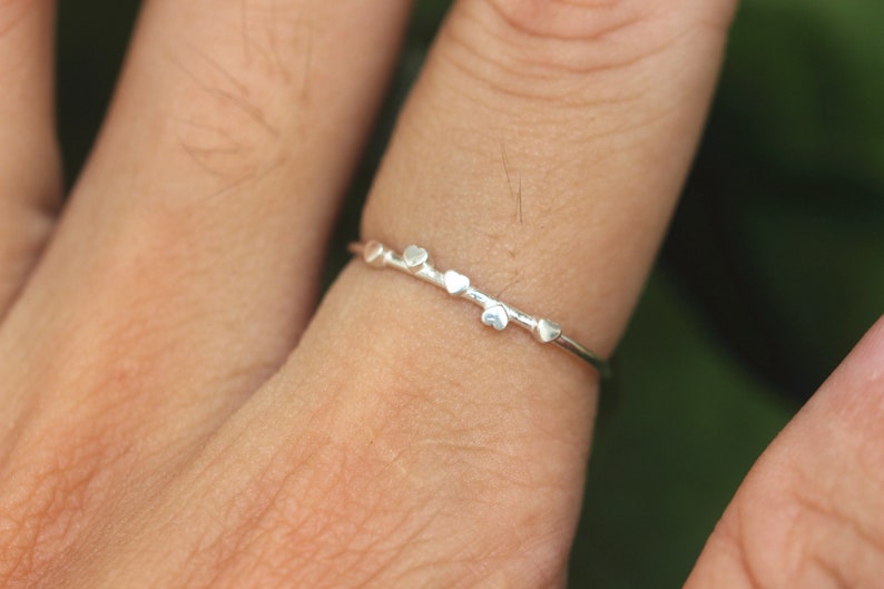 K&ouml;nnte beinhalten: Ein silberner Ring mit einem zarten Band und f&uuml;nf kleinen herzf&ouml;rmigen Anh&auml;ngern.
