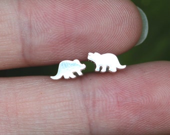 May include: A pair of silver earrings shaped like a dinosaur, likely a Triceratops.