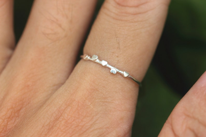 K&ouml;nnte beinhalten: Ein silberner Ring mit einem zarten Design mit kleinen herzf&ouml;rmigen Akzenten.