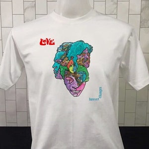 May include: White t-shirt featuring a colourful graphic of four faces and the word "LOVE" in red. The text "forever" and "changes" are also printed on the shirt.