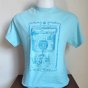 May include: A light blue t-shirt featuring a blue graphic that reads "SPAMalo" with text that says "Longwood High School Proudly Presents". The graphic includes a can of Spam and a drum.