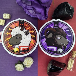 May include: Two round stickers with a stained glass design. One sticker features a black sheep with a halo and the other features a white sheep with a halo. Both stickers have a purple and red background.