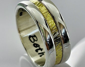 Puede incluir: Una banda de boda de plata y oro con una incrustación de oro texturizada. La banda está inscrita con la palabra "Both".