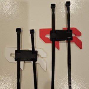 May include: Three black cable tie organizers with different colored mounting brackets. One has a white bracket, another has a red bracket, and the third has a white bracket. The organizers are mounted on a beige wall.