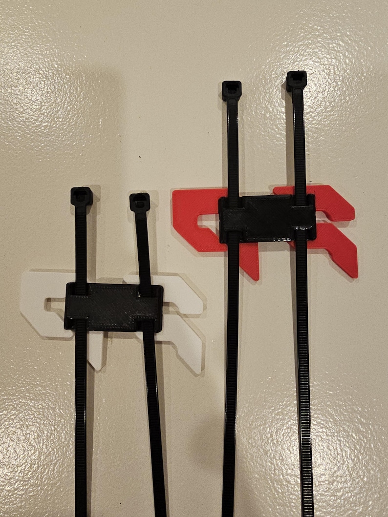 May include: Three black cable tie organizers with different colored mounting brackets. One has a white bracket, another has a red bracket, and the third has a white bracket. The organizers are mounted on a beige wall.