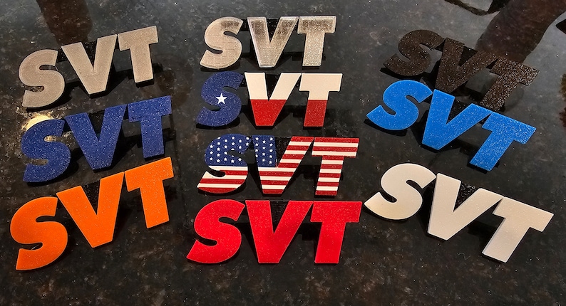 May include: A collection of various SVT logo designs in different colors and patterns. The logos include solid colors like orange, red, and blue, as well as designs featuring the American and Texas flags. The logos are displayed on a dark surface.