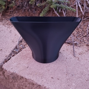 May include: A black plastic funnel with a wide opening and a narrow spout. The funnel is sitting on a concrete surface.