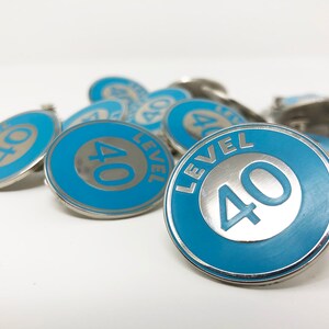 May include: A close-up of several blue and silver metal pins with the text "LEVEL 40" on them.