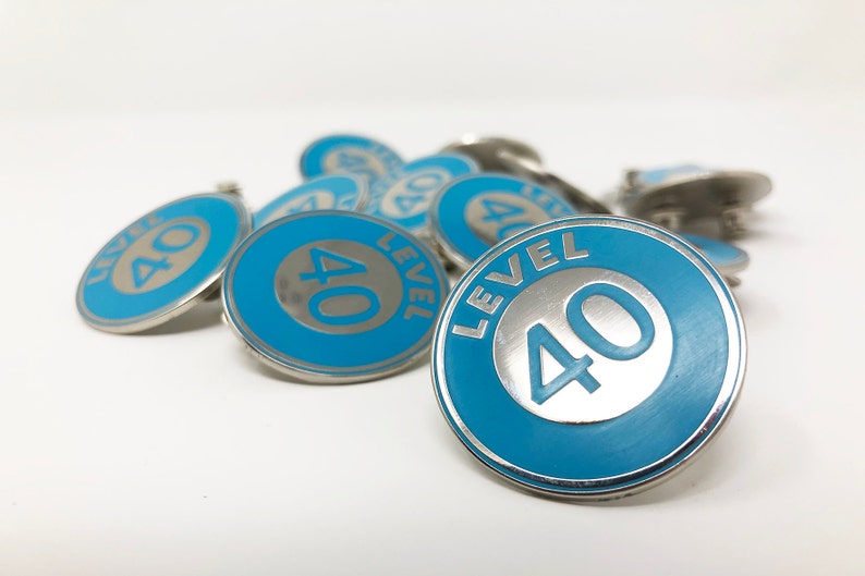 May include: A close-up of several blue and silver metal pins with the text "LEVEL 40" on them.