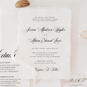 May include: Elegant wedding invitation suite featuring calligraphy text on textured white paper. Includes invitation, details, RSVP card with QR code, and pearl bracelet. The main invitation lists the names Jessica Madison Hughes and Adam Edward Lewis.