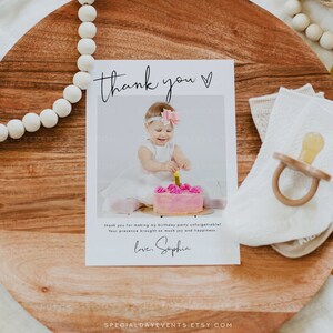 May include: A thank you card with a photo of a baby girl in a white dress, holding a lit candle on a pink cake. The card reads "thank you" and includes a personal message and signature.