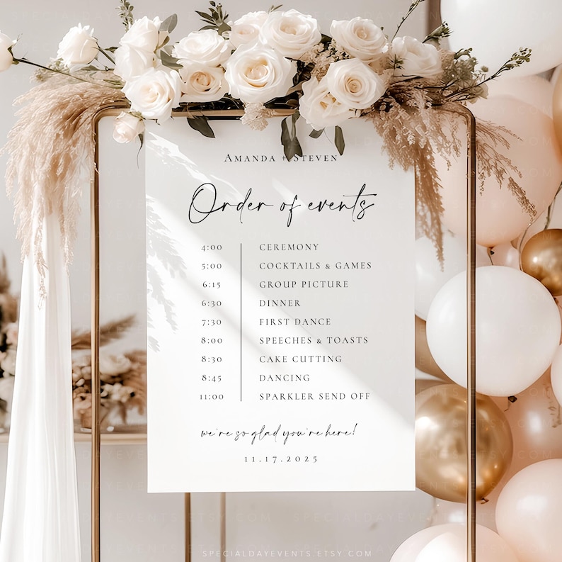 May include: A wedding event sign with the text "Order of events" and a schedule. The sign is decorated with white roses and pampas grass. The sign is on a gold metal frame, with balloons in the background.