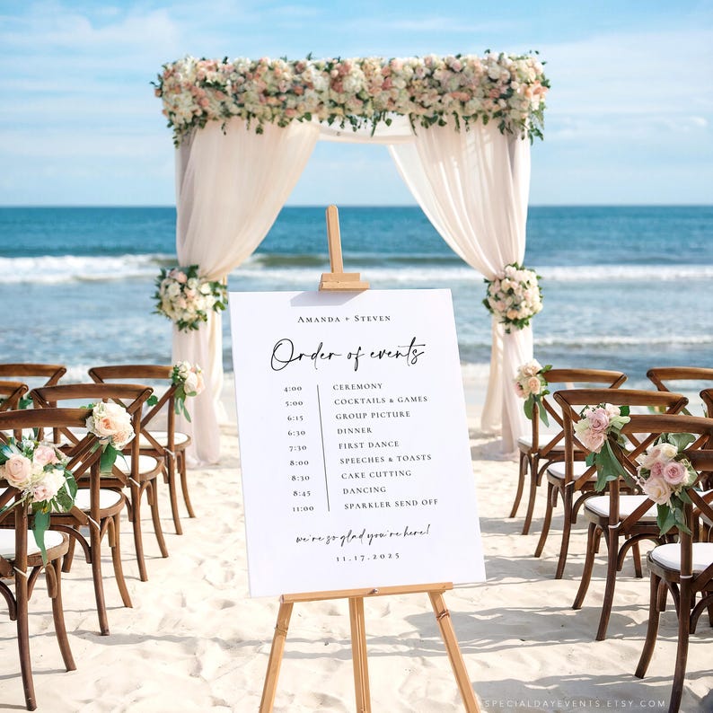 May include: A beach wedding ceremony setup with a white sign displaying the order of events. The sign is on a wooden easel, with wooden chairs and floral arrangements. A floral arch and sheer fabric frame the ocean backdrop.