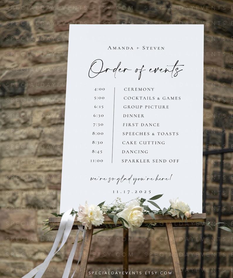 May include: A white wedding sign on a wooden easel, displaying the order of events for Amanda and Steven's wedding. The sign includes the date, time, and activities, with floral and ribbon accents at the base.