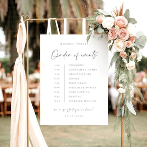May include: A wedding event sign with the names "AMANDA + STEVEN" and the words "Order of events" in elegant script. The sign lists the schedule, including the ceremony, dinner, and dancing. The sign is decorated with flowers and ribbons.
