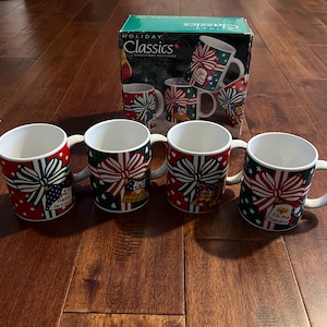 May include: Set of four white ceramic mugs with Christmas-themed designs. Each mug features a red and green bow with a gift tag. The tags have different holiday greetings, including "Happy Holidays", "Joy to the World", "Tis the Season", and "Merry Christmas".