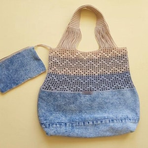Può includere: Una borsa tote e una piccola pochette abbinata. La borsa presenta una base in denim lavato all'acido, una sezione centrale in uncinetto a trama aperta blu e beige e manici in uncinetto beige. La piccola pochette rettangolare è in denim.