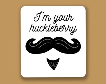 Könnte beinhalten: Ein weißer quadratischer Aufkleber mit dem Text "I'm your huckleberry" in schwarzer Schrift. Darunter ein schwarzer Schnurrbart und ein kleiner schwarzer Ziegenbart. Der Hintergrund ist einfarbig braun.