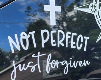 May include: A white vinyl decal with a cross and the text "NOT PERFECT just forgiven" on a black car window.