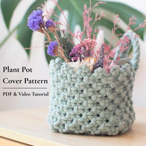 Peut inclure: Un cache-pot crocheté vert sauge avec un bord supérieur festonné, contenant un bouquet de fleurs séchées violettes, roses et blanches. Le texte "Plant Pot Cover Pattern" et "PDF & Video Tutorial" est imprimé sur le côté gauche.
