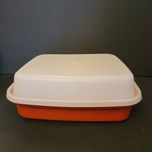 May include: A square, orange food storage container with a white lid. The lid has a slightly textured surface and fits snugly on the container. The container is made of durable plastic and is designed for food storage.