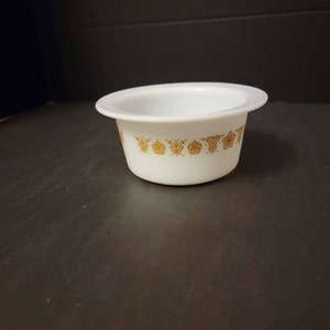 May include: White ceramic bowl with a gold floral pattern around the rim. The bowl is slightly wider at the top than the bottom.