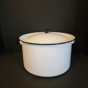 May include: White enamelware pot with a black rim and a black knob on the lid. The pot has two handles.