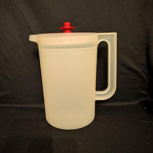 May include: A white ceramic mug with a black handle and the text "But First, Coffee" in a bold, black font. The mug is set against a blurred background, suggesting a cozy setting.
